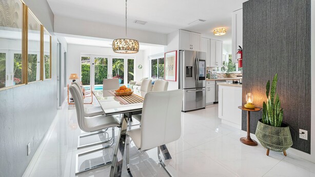 A modern kitchen with stainless steel appliances, a dining area with a glass table, and a large window offering a view of greenery. - Remodeled Mid-century home with pool, hot tub & EV charger (Wilton Manors)