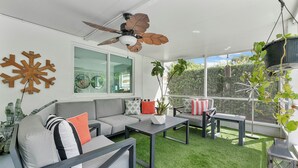 A modern outdoor living space with a ceiling fan, a large window, and a green artificial turf floor. - Remodeled Mid-century home with pool, hot tub & EV charger (Wilton Manors)