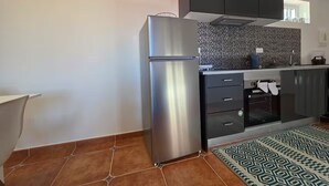 A kitchen with a stainless steel refrigerator, dark cabinets, a tiled backsplash, and a patterned rug. - Elena's corner (Funchal)