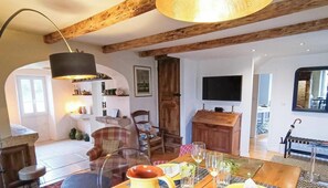 Una sala de estar acogedora con chimenea, vigas de madera, una mesa de comedor con vasos y un televisor montado en la pared.