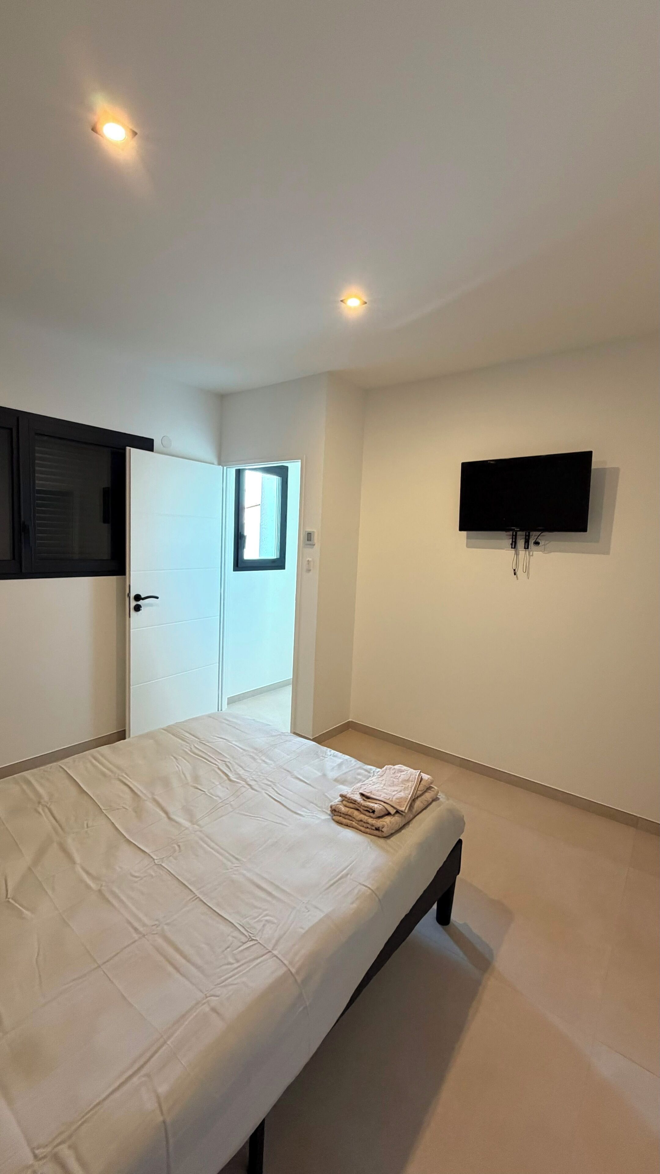 A bedroom with a bed, a TV mounted on the wall, and a door leading to another room.