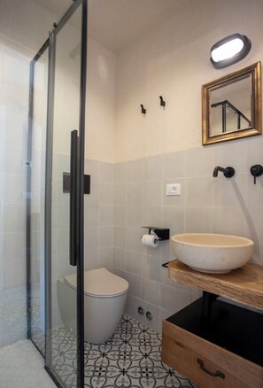Un baño moderno con cabina de ducha de vidrio, inodoro, lavabo con encimera de madera y espejo con marco dorado.