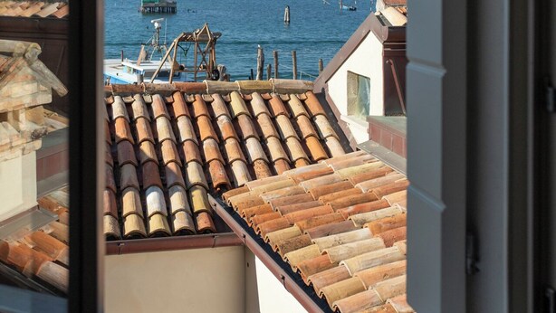 A view through a window of a coastal building with a tiled roof, a boat docked nearby, and the sea in the background.