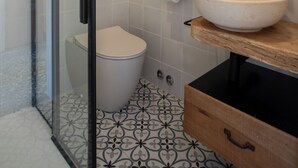Een badkamer met een douchecabine van glas, een toilet, een wastafel met houten blad, een spiegel en vloertegels met een patroon.