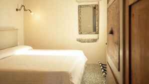 Een slaapkamer met een bed, een houten kledingkast, een klein raam en een wandlamp.