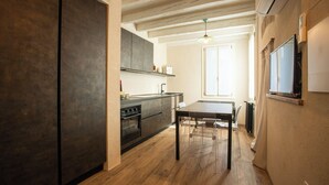 Een moderne keuken met donkere kastjes, een houten vloer en een eethoek met een tafel en stoelen.