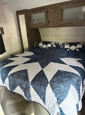 Un lit avec une tête de lit matelassée et une fenêtre avec un store à motifs.