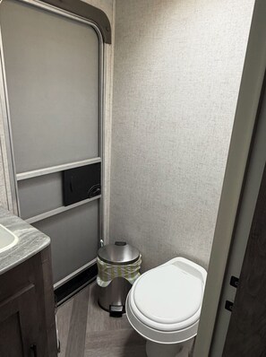 Une petite salle de bain comprenant des toilettes, une petite poubelle et un meuble avec un lavabo.