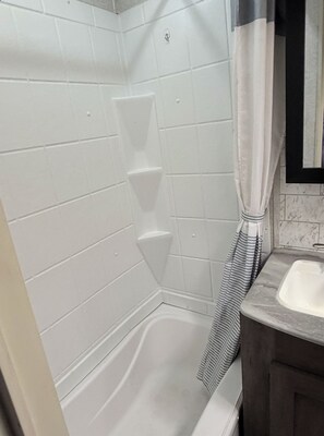 Une salle de bain aux murs recouverts de carreaux blancs, une douche avec une serviette à rayures et un lavabo doté d'un plan de travail en marbre.