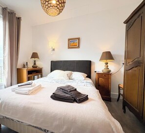 Ein ordentlich bezogenes Bett mit gefalteten Handtüchern, zwei Nachttischlampen, ein gerahmtes Bild an der Wand und ein Kleiderschrank.