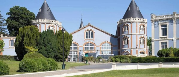 Un grande edificio con due torri imponenti, un ingresso centrale con finestre ad arco e un giardino curato.