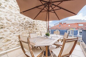 Un tavolo in legno con sedie e un ombrellone, di fronte a un muro in pietra e vista su edifici.