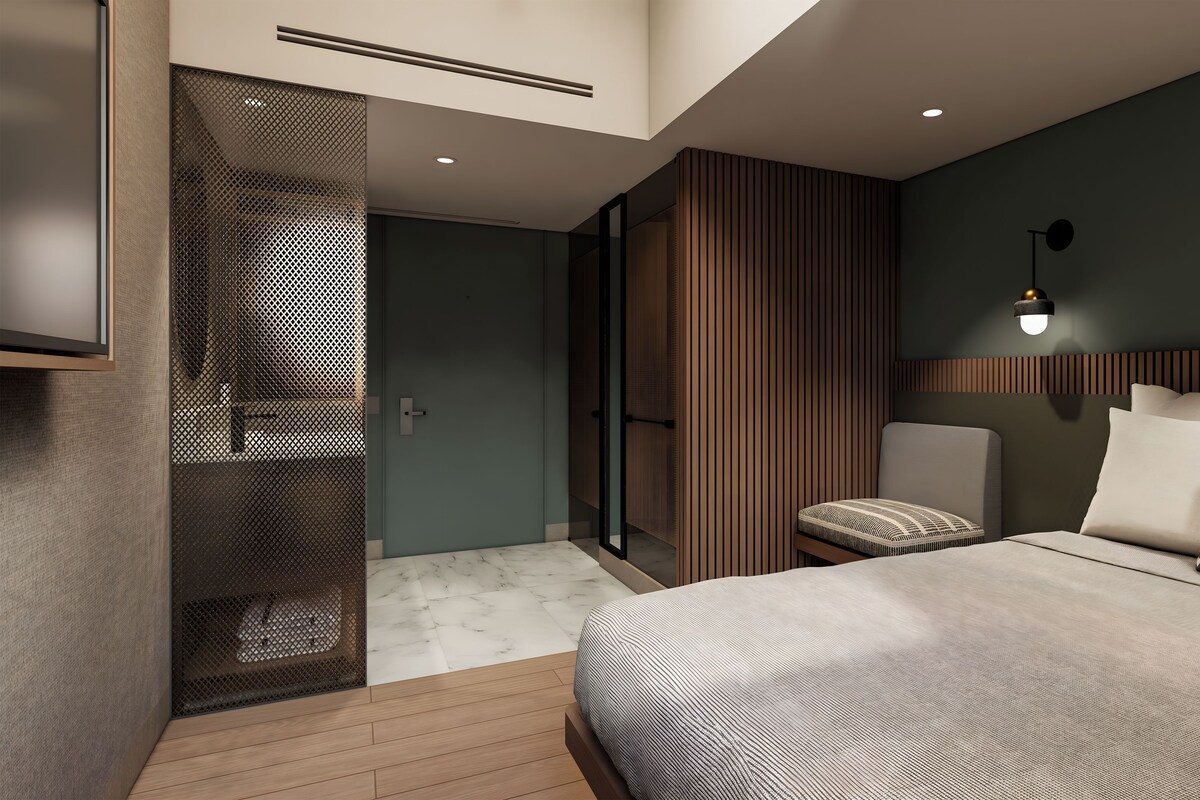 A modern bedroom with a bed, a chair, a wall-mounted light, and a framed picture.