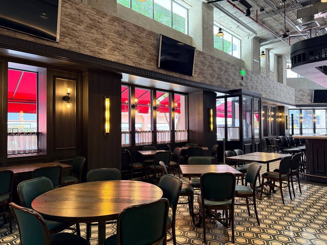 Un restaurant avec de hauts plafonds, des murs en briques apparentes et de grandes fenêtres. Les tables et les chaises sont disposées pour accueillir les clients.
