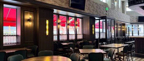 Un restaurant avec de hauts plafonds, des murs en briques apparentes et de grandes fenêtres. Les tables et les chaises sont disposées pour accueillir les clients.