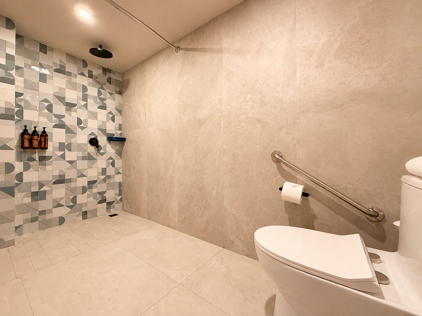 A modern bathroom with a shower, toilet, and handrails.