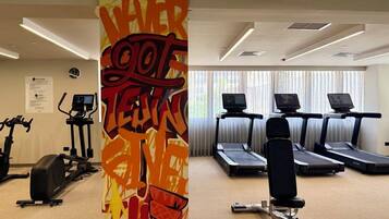 Un gimnasio con cintas de correr, bicicletas estáticas y una pared con un diseño abstracto y colorido.