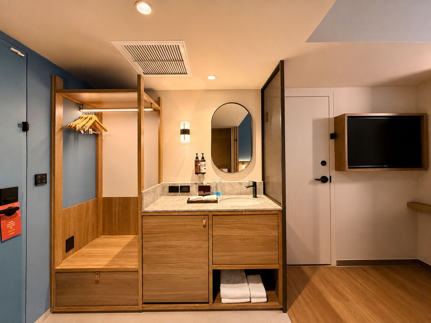 Een moderne badkamer met een houten wastafelmeubel, een grote spiegel en een ingebouwde televisie.
