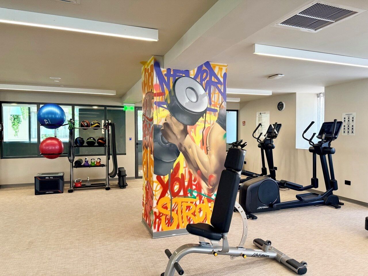 A gym with exercise equipment, a wall with a colorful mural, and a treadmill.