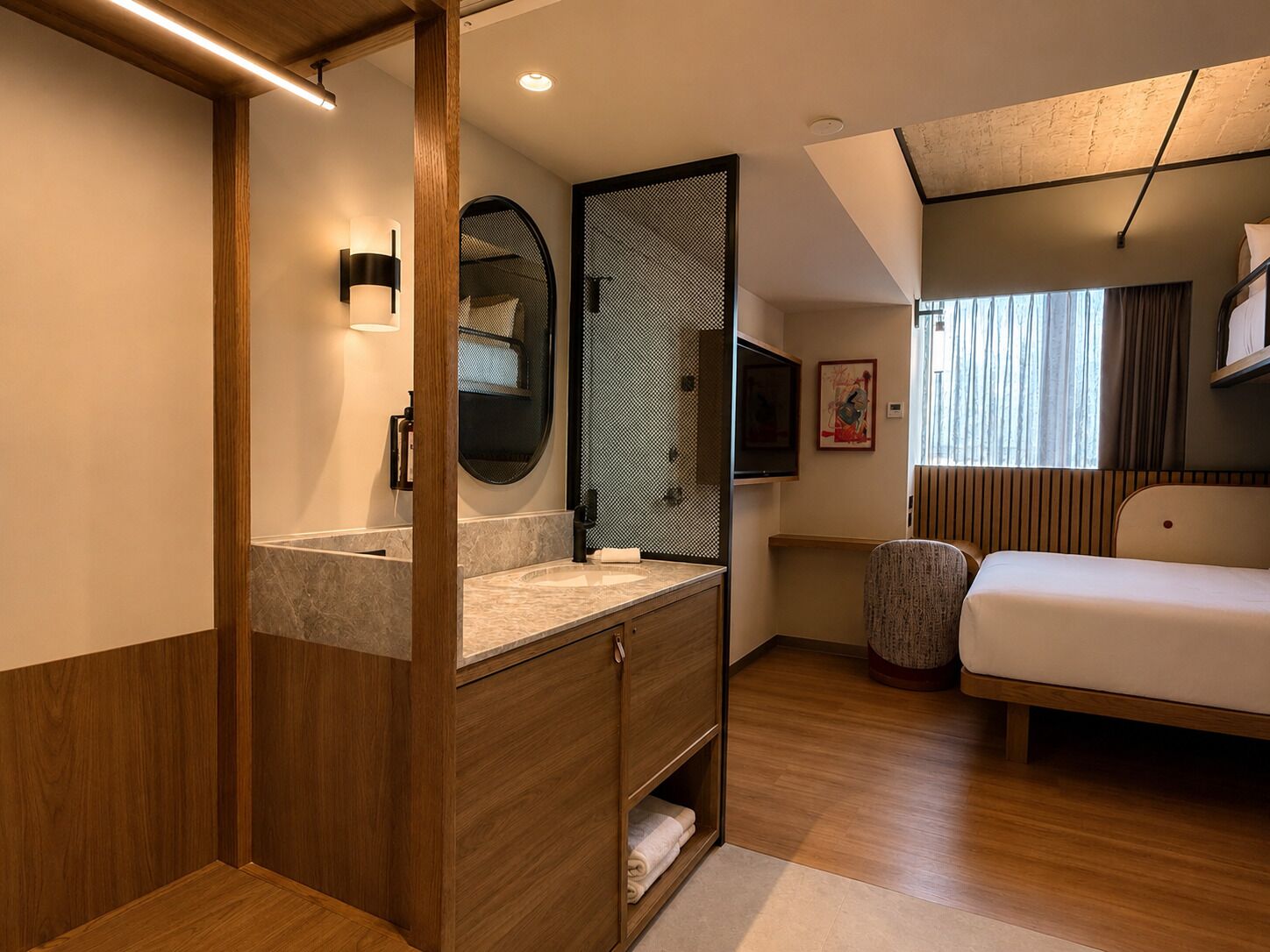 Een moderne hotelkamer met een houten wastafel, een ronde spiegel, een bed, een televisie en een raam met gordijnen.