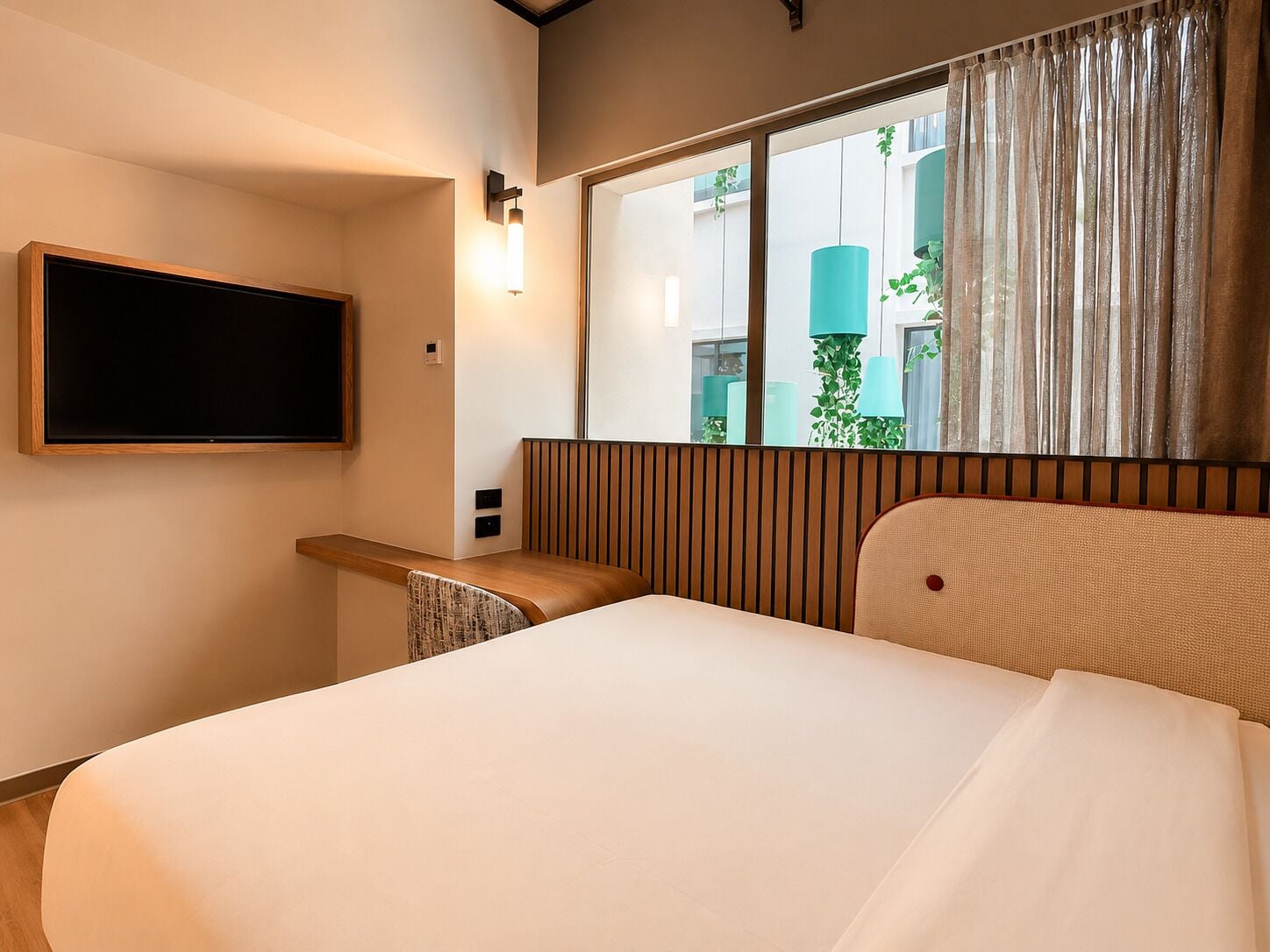 A hotel room with a bed, a television mounted on the wall, and a window with curtains.