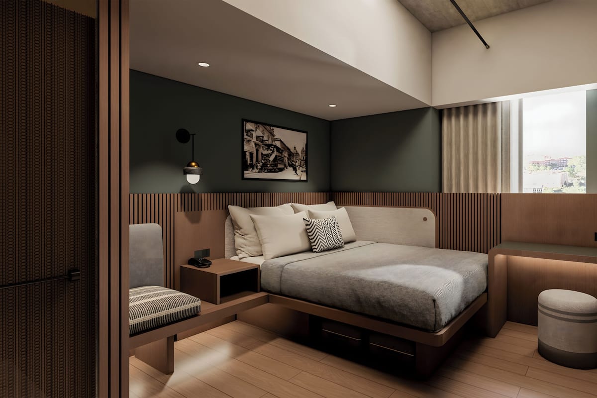A modern bedroom with a bed, bedside tables, a chair, a small stool, a window with curtains, and a wall-mounted light fixture.