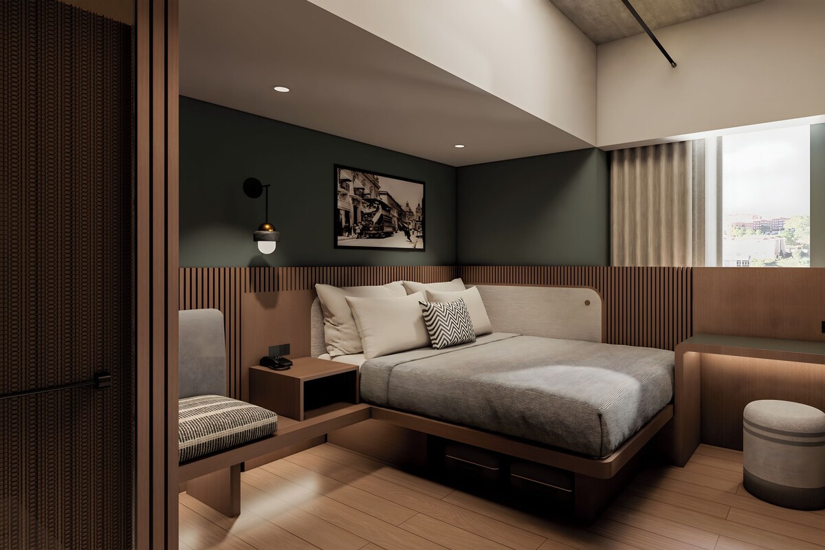 A modern bedroom with a bed, bedside tables, a chair, a small stool, a window with curtains, and a wall-mounted light fixture.