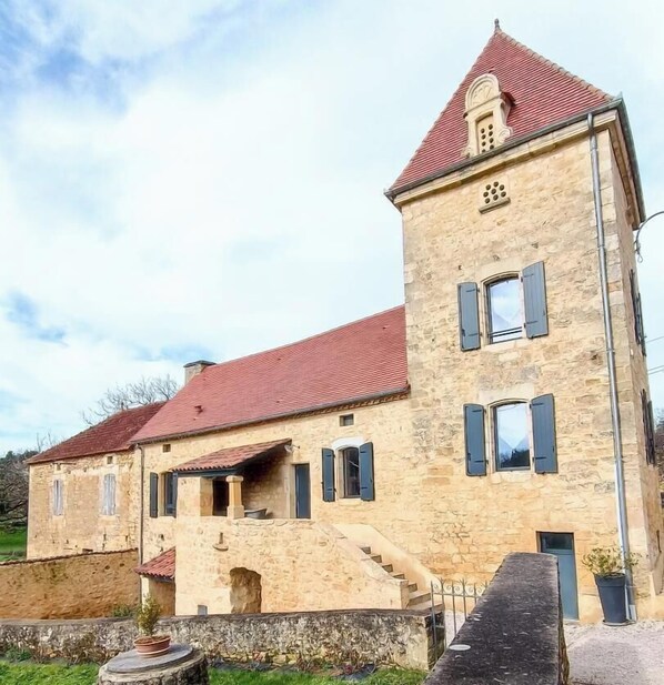 Ein Steinhaus mit rotem Dach, einem Turm mit Uhr und einer Treppe zum Eingang.