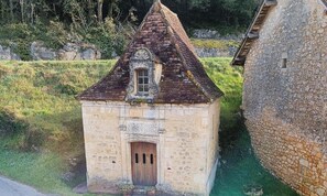 A stone building with a pitched roof, a small window, and a wooden door. - Gîtes de France® - Les Deux Plumes (PAYRIGNAC)