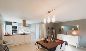 Eine moderne Küche mit weißen Schränken, einem Essbereich mit Tisch und Stühlen sowie einem großen Fenster.