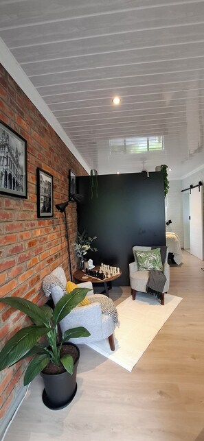 Un salon moderne avec un mur en briques, un mur d’accent noir et un plancher en bois. On y trouve deux fauteuils, une table basse et une plante en pot.