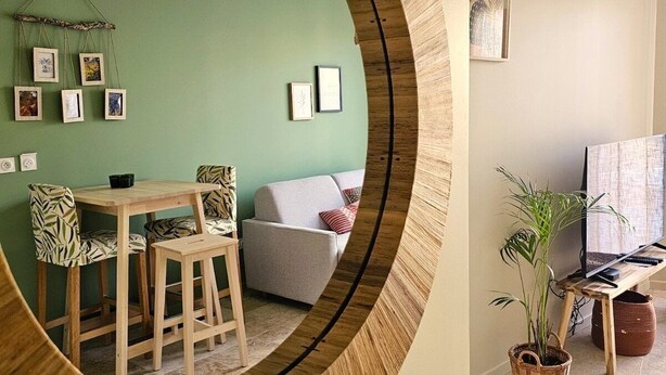 Una sala de estar con un espejo redondo, una mesa de comedor con sillas, un sofá y un mueble de televisión con una planta.