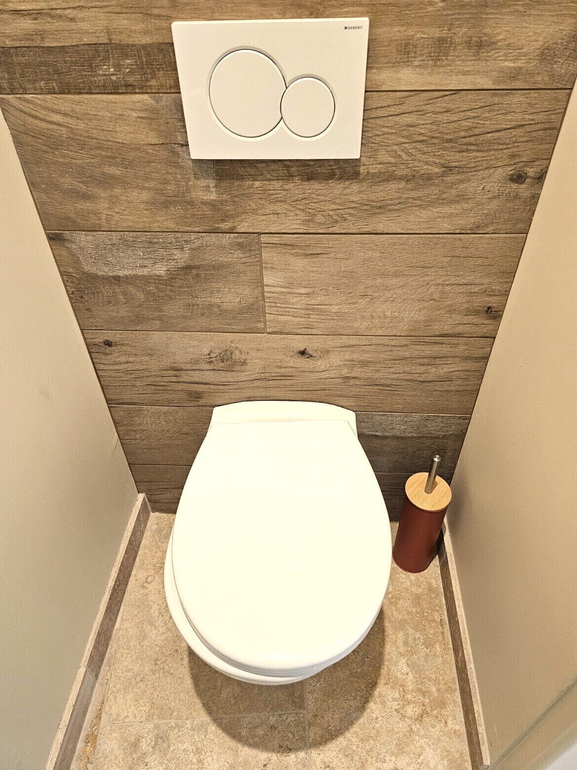 A small, modern bathroom with a wooden wall, a white toilet, and a toilet brush.