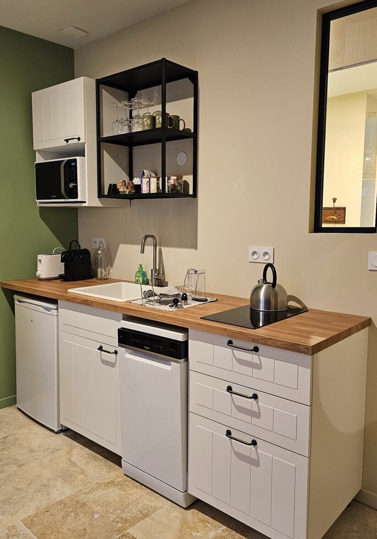 Cocina pequeña con armarios blancos, encimera de madera, microondas integrado, hervidor y un estante con cristalería.
