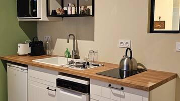 Cocina pequeña con armarios blancos, encimera de madera, microondas integrado, hervidor y un estante con cristalería.