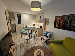 Un salon moderne avec un canapé vert, un coin repas doté de tabourets de bar et un espace cuisine.