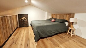 A bedroom with a wooden floor, a bed with a green bedspread, a wooden headboard, and a wall-mounted lamp. - Le Chalet-Loft-Private Bathroom-Apartment-Garden view (Genas)