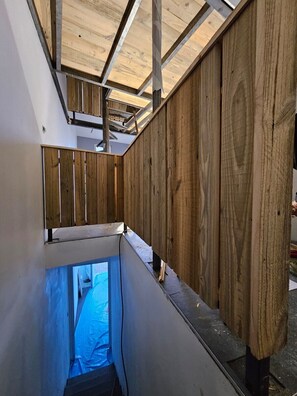Un étroit escalier intérieur, fermé, avec un lambris en bois et une structure en poutres métalliques.