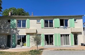 Un immeuble de deux étages avec des volets verts, un petit balcon et un arbre dans le jardin.