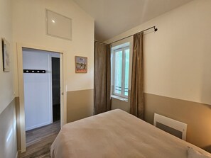 Ein Schlafzimmer mit Bett, einem Vorhangfenster, einem Heizkörper und einer Tür zu einem anderen Raum.