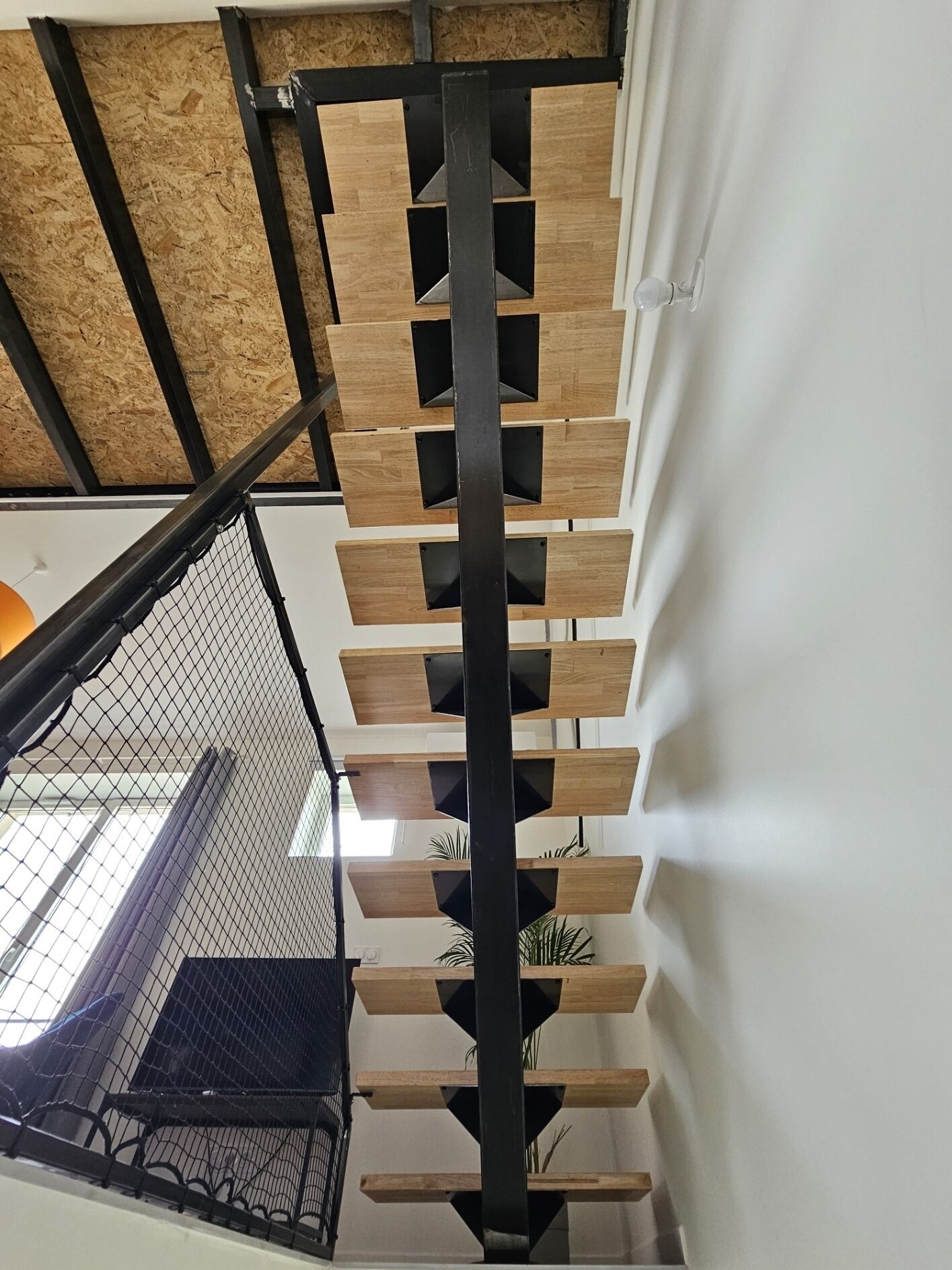 Una escalera moderna con escalones de madera y barandillas de metal negro, que desciende a un nivel inferior.