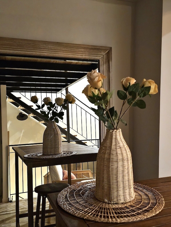A room with a staircase, a table with a woven placemat, and two vases with yellow roses.