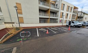 Un immeuble résidentiel à plusieurs étages doté de balcons, une zone de stationnement avec des emplacements délimités et un fourgon blanc garé à proximité.