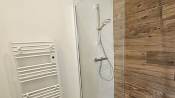 Ein modernes Badezimmer mit Duschkabine aus Glas, Holzvertäfelung und einem weißen Handtuchhalter.