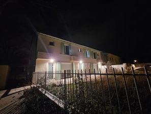 A two-story building with a gated entrance and multiple windows, illuminated by exterior lighting.