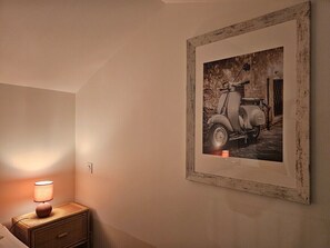 Ein gerahmtes Foto eines alten Rollers an der Wand, eine Nachttischlampe und ein Nachttisch aus Holz.