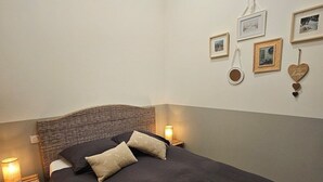 Une chambre avec un grand lit, une tête de lit en osier, des lampes de chevet et des tableaux encadrés accrochés au mur.