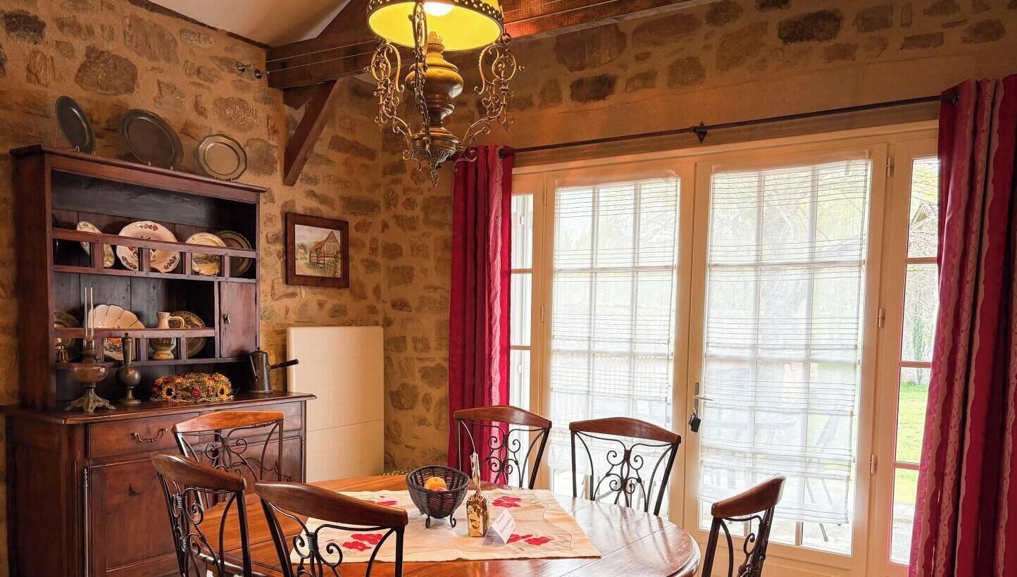 A dining area with a table, chairs, a chandelier, and a window with curtains.