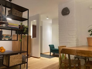 A modern living room with a wooden floor, a dining table, a bookshelf, and a green chair.