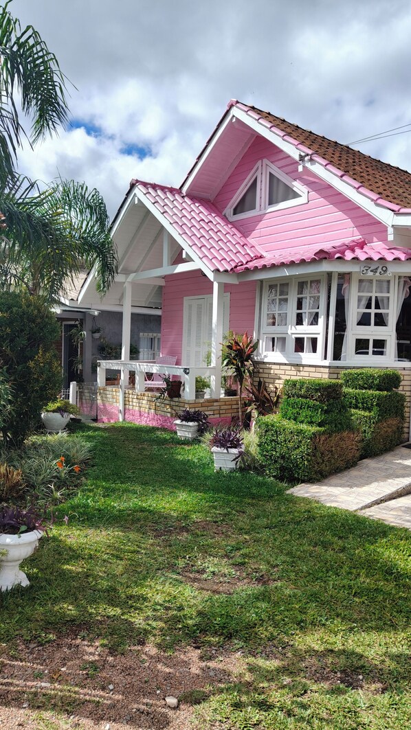 A pink house with a tiled roof, a porch with a bench, and a well-maintained garden.